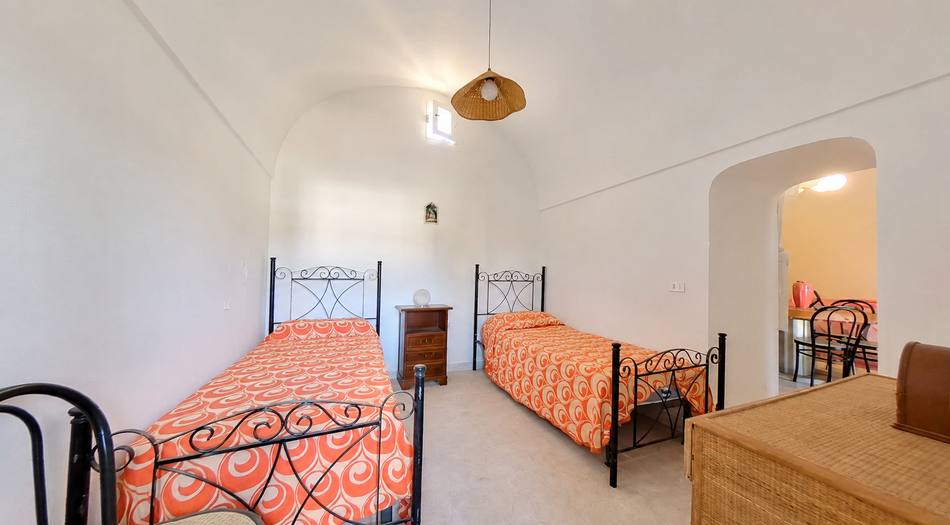 The vaulted bedroom today: two wrought-iron beds, orange bedspread, walnut bedside table