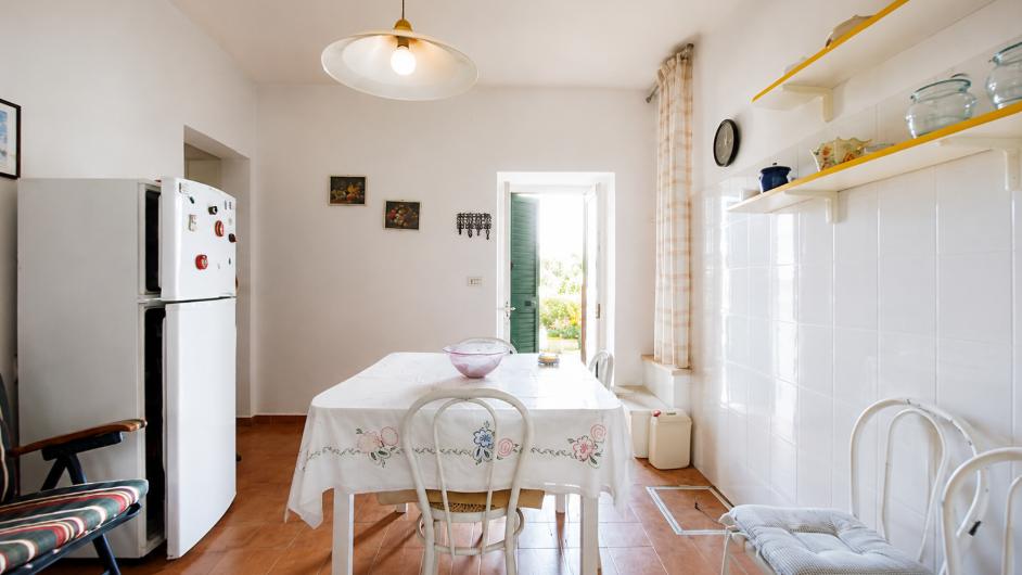 The kitchen today: white tiles, table with an embroidered cloth, door onto the garden