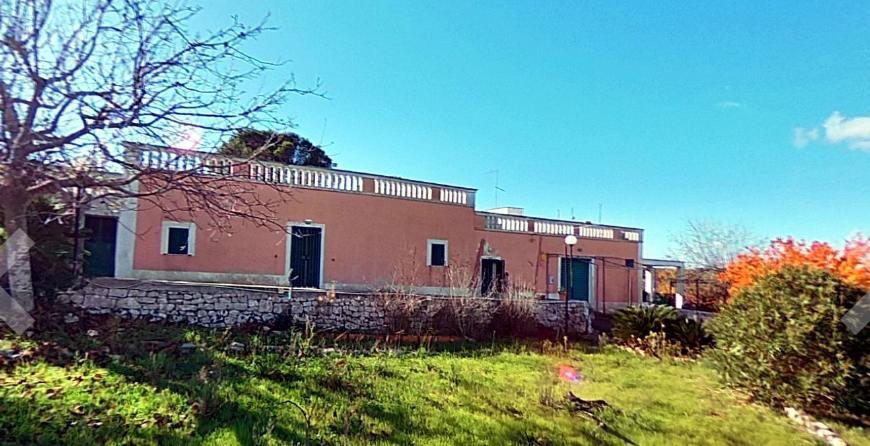 The house today seen from the garden: pink render, dry-stone wall and uncut grass